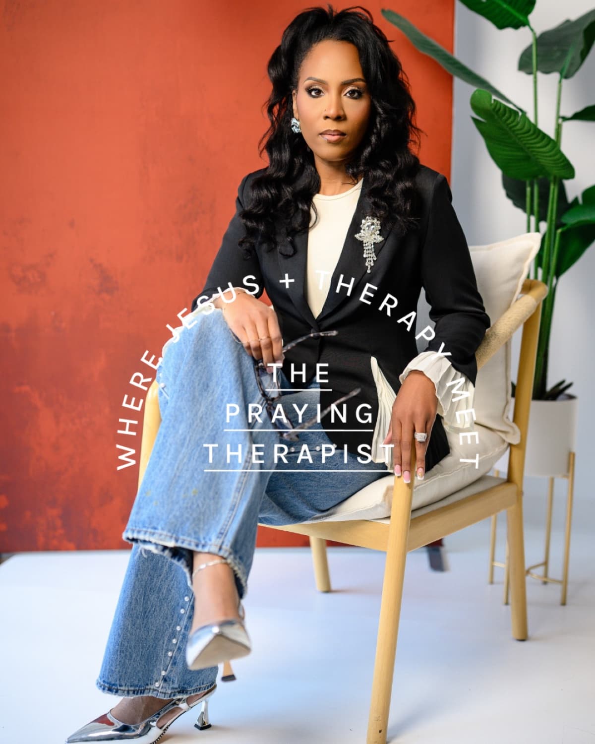 Yvonne Sailor-Walker seated in a chair against a warm terracotta wall, wearing a black blazer